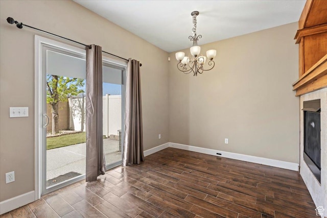 unfurnished dining area with dark wood-style flooring, baseboards, a chandelier, and a fireplace