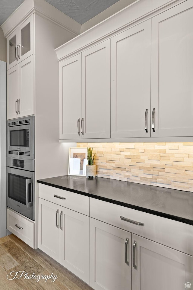kitchen featuring dark countertops, white cabinets, decorative backsplash, stainless steel appliances, and wood finished floors
