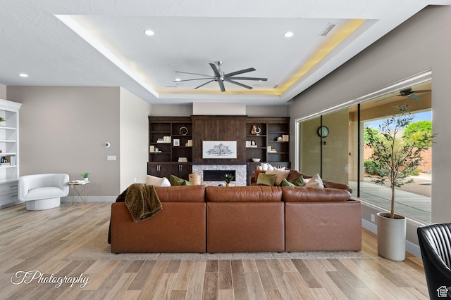 living area featuring a raised ceiling, wood finished floors, a ceiling fan, and baseboards
