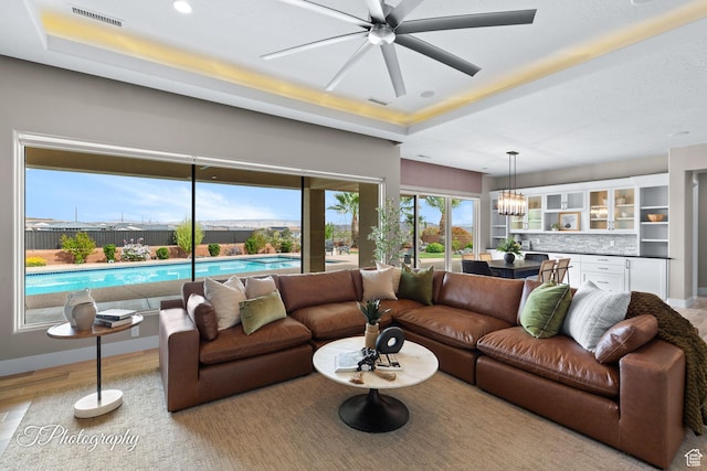 living area with a tray ceiling, visible vents, a ceiling fan, and baseboards
