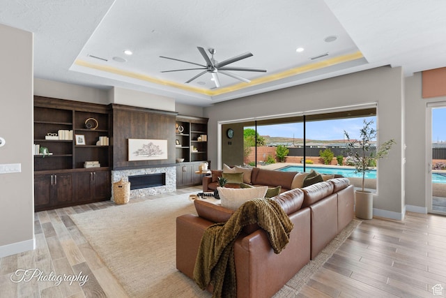 living room with ceiling fan, baseboards, a tray ceiling, and visible vents