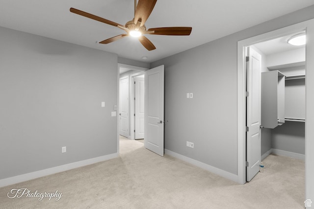 unfurnished bedroom with a walk in closet, baseboards, a ceiling fan, and carpet