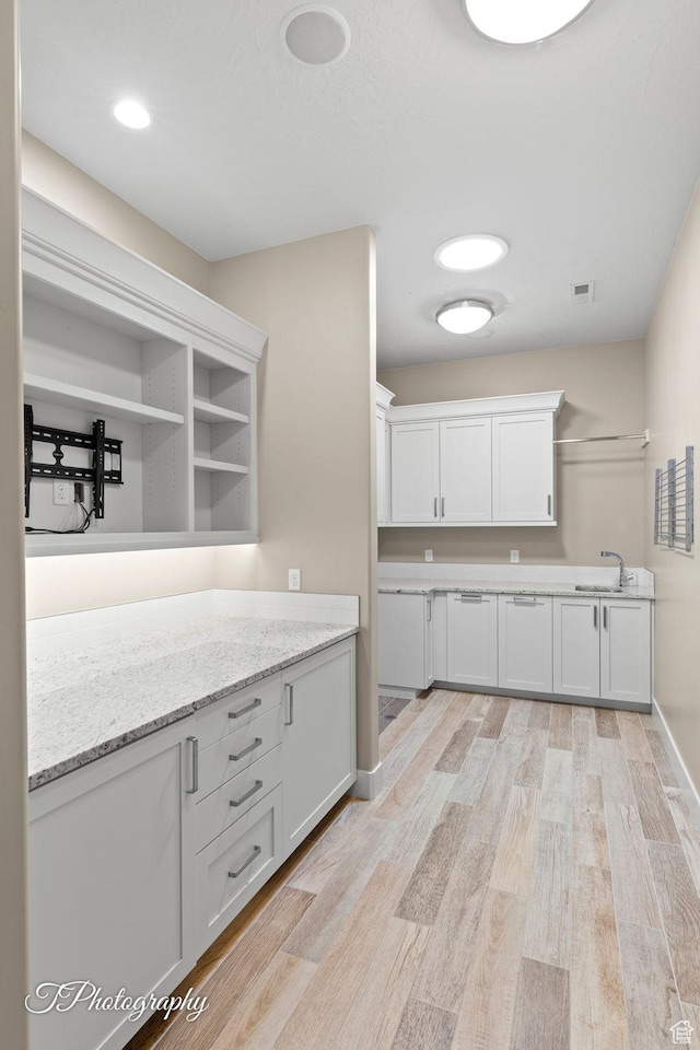 kitchen with light wood-style floors, open shelves, visible vents, white cabinets, and a sink