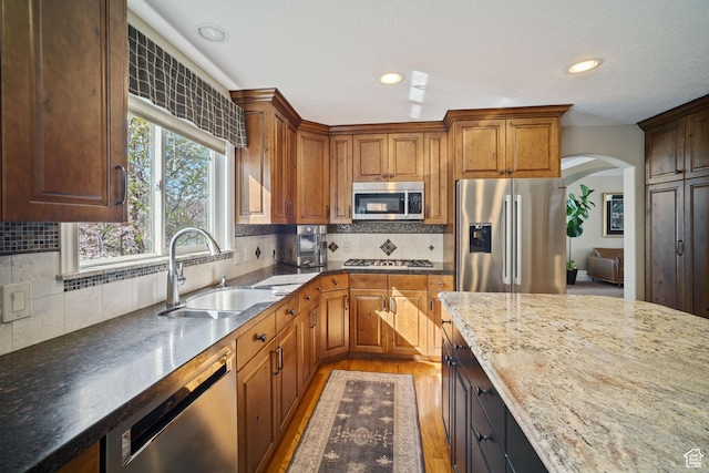1778 E Indian Wells Ln, Draper, UT 84020 - kitchen featuring light wood-style floors, dark stone counters, arched walkways, appliances with stainless steel finishes, and a sink