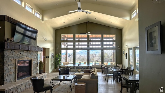 living room with wood finished floors, a ceiling fan, high vaulted ceiling, and a stone fireplace