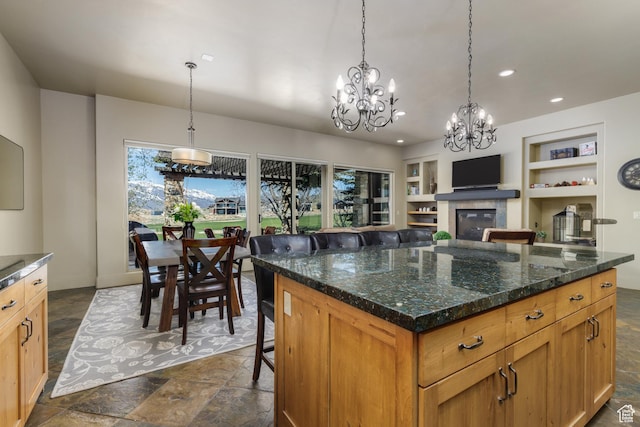kitchen with pendant lighting, built in features, stone finish floor, a glass covered fireplace, and a notable chandelier