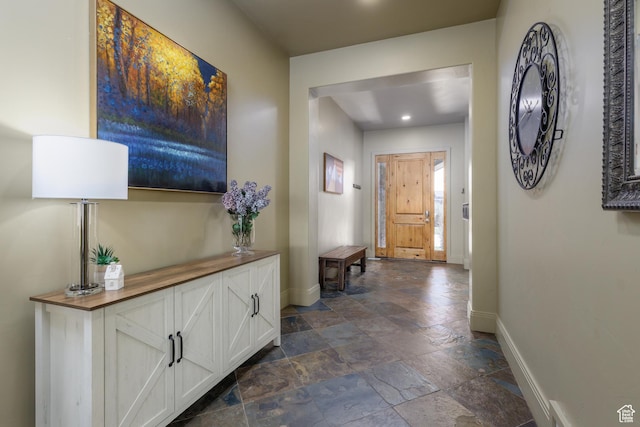 hall featuring stone tile flooring and baseboards