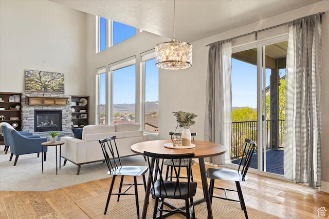 dining space with a stone fireplace, light wood finished floors, plenty of natural light, and a chandelier