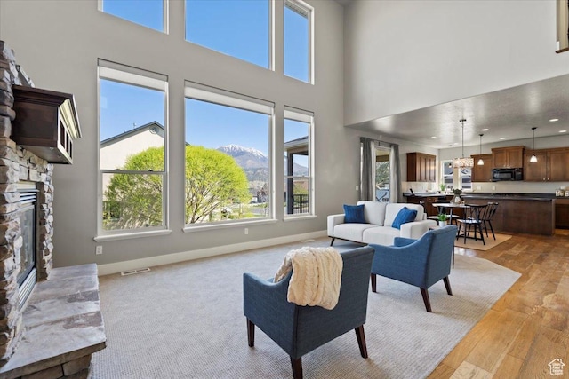 living area featuring a wealth of natural light, a stone fireplace, a high ceiling, and light wood-style flooring