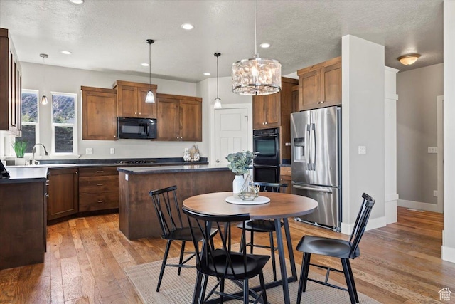 kitchen featuring light wood-type flooring, black appliances, a center island, a sink, and decorative light fixtures