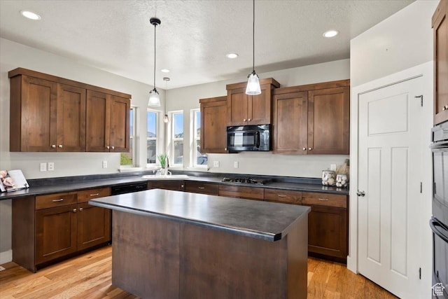 kitchen with light wood-type flooring, black microwave, dark countertops, stainless steel gas cooktop, and a sink