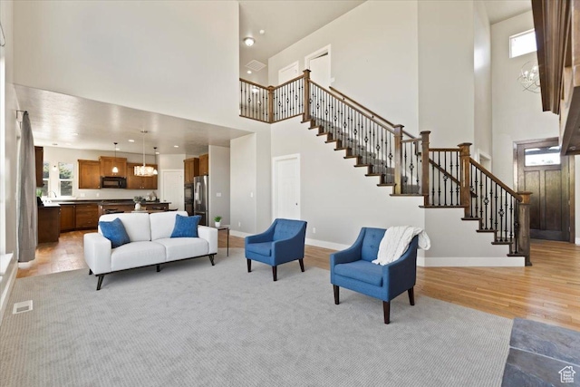 living room with a towering ceiling, baseboards, stairs, visible vents, and light wood finished floors