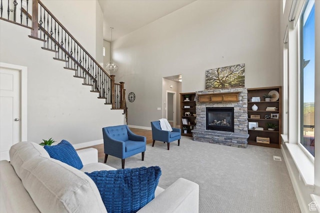 living area with baseboards, a high ceiling, a stone fireplace, carpet, and stairway
