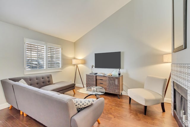 living room with a tile fireplace, baseboards, lofted ceiling, and wood finished floors