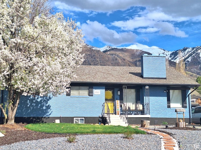 single story home with brick siding, a mountain view, a chimney, and covered porch
