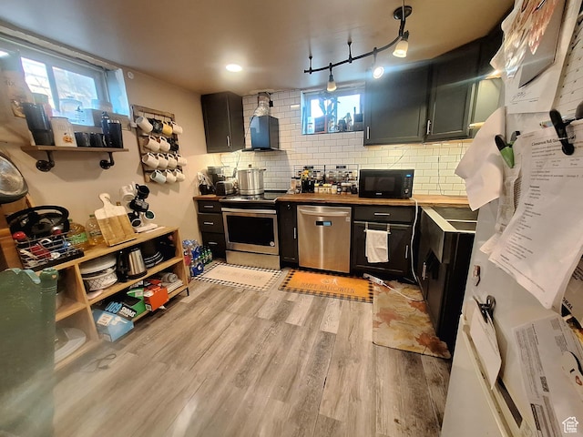 3150 N Iowa Ave W, Ogden, UT 84403 - kitchen with light wood-style floors, wall chimney range hood, stainless steel appliances, dark cabinetry, and decorative backsplash
