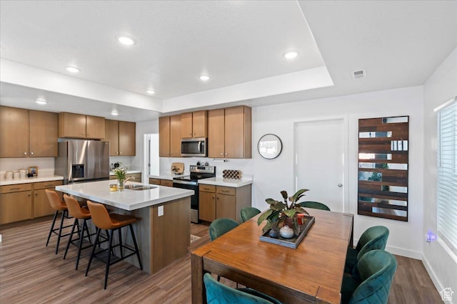 kitchen with visible vents, light countertops, wood finished floors, stainless steel appliances, and a breakfast bar area