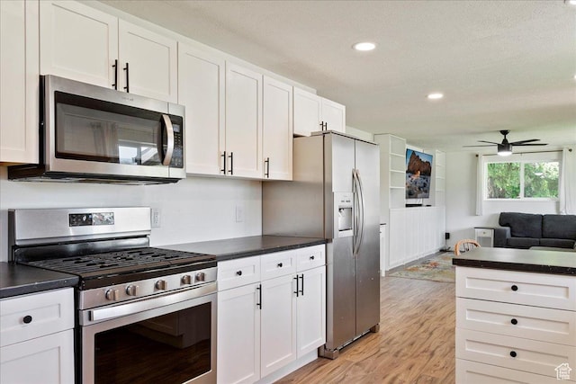 kitchen with appliances with stainless steel finishes, ceiling fan, dark countertops, and white cabinets