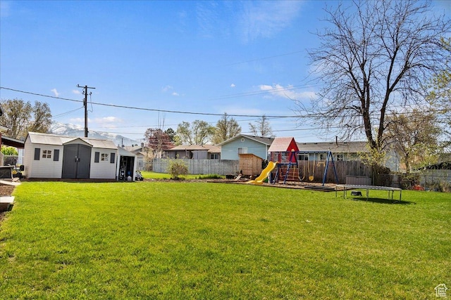view of yard with a trampoline, a fenced backyard, a playground, and an outbuilding