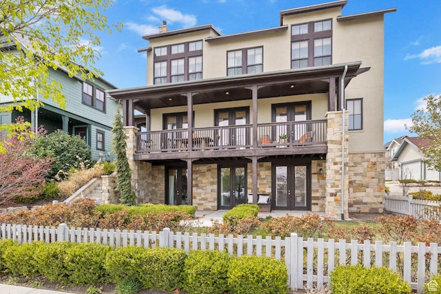 view of front facade featuring a fenced front yard, french doors, stone siding, and stucco siding