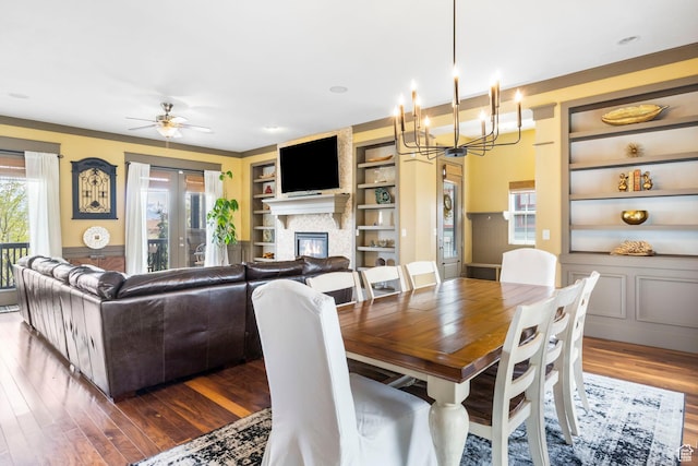 dining room featuring a large fireplace, built in features, wood finished floors, and ceiling fan with notable chandelier
