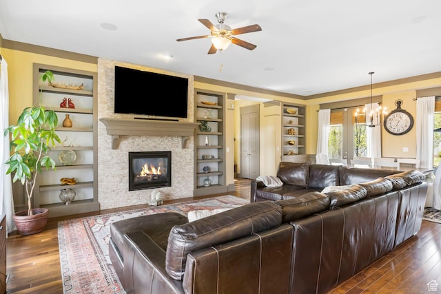 living area with a large fireplace, built in shelves, ceiling fan with notable chandelier, and dark wood finished floors