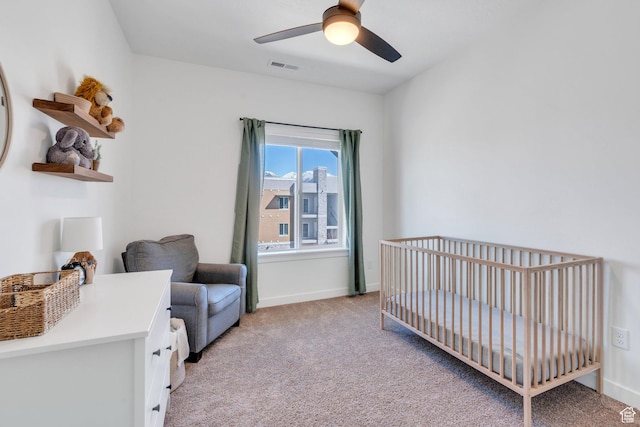 bedroom with baseboards, a crib, a ceiling fan, visible vents, and light colored carpet