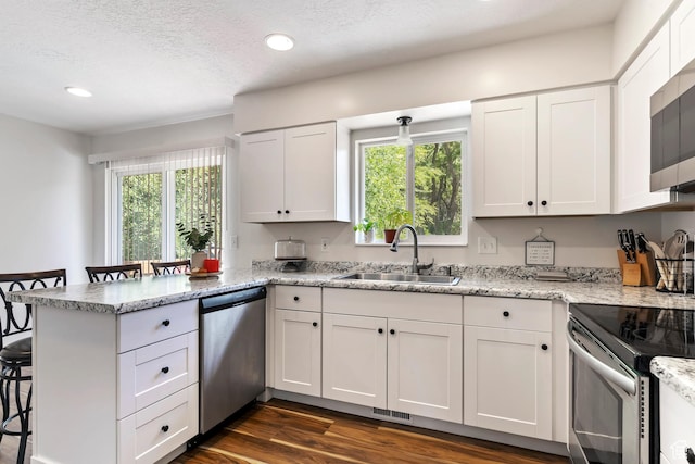 kitchen with a peninsula, white cabinetry, a breakfast bar area, stainless steel appliances, and a sink