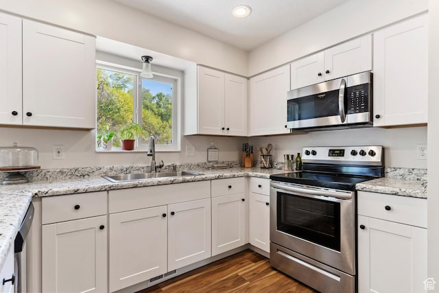 kitchen with dark wood finished floors, light stone countertops, white cabinets, appliances with stainless steel finishes, and a sink