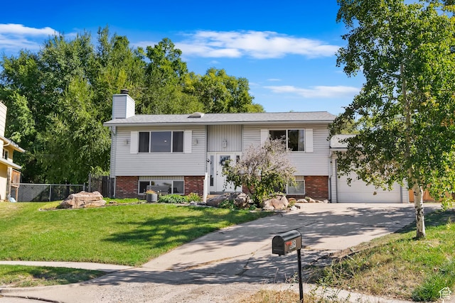 raised ranch with a garage, fence, concrete driveway, brick siding, and a front lawn
