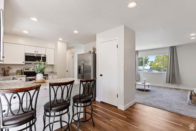 kitchen with a kitchen breakfast bar, recessed lighting, a peninsula, white cabinetry, and appliances with stainless steel finishes