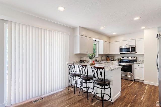 kitchen featuring a breakfast bar area, white cabinetry, a peninsula, and stainless steel appliances