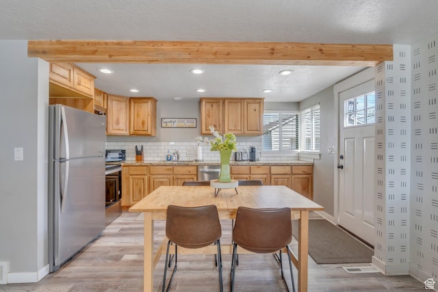 kitchen with a sink, appliances with stainless steel finishes, light brown cabinetry, light wood-style floors, and beam ceiling