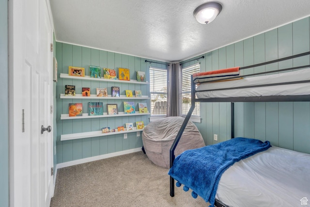 bedroom with wood walls, carpet, a textured ceiling, and baseboards