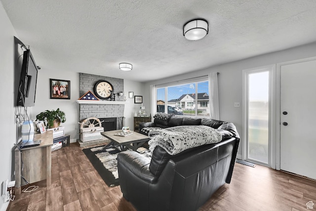 living area featuring a brick fireplace, a textured ceiling, baseboards, and wood finished floors