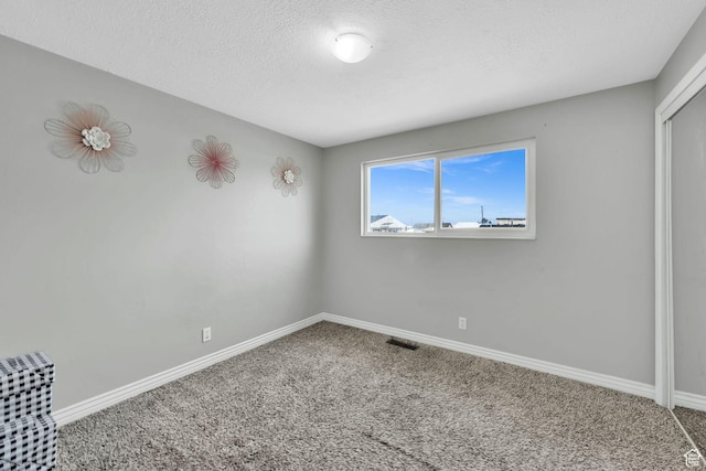 unfurnished bedroom with a textured ceiling, carpet flooring, baseboards, and visible vents
