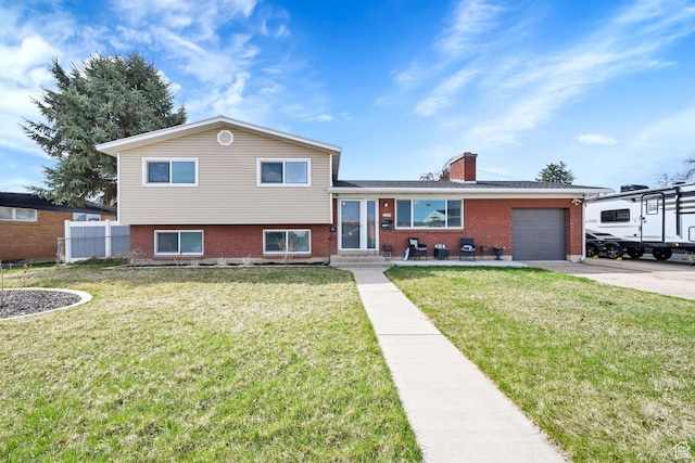 tri-level home featuring a front yard, a garage, a chimney, concrete driveway, and brick siding