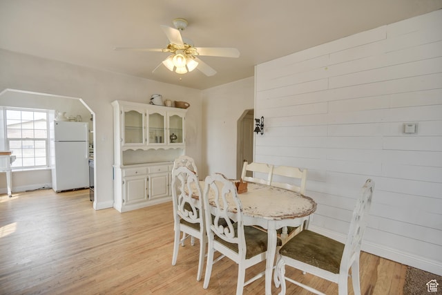 dining area with ceiling fan, light wood-type flooring, arched walkways, and baseboards