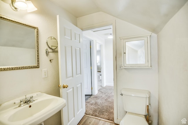 half bathroom with toilet, wood finished floors, a sink, and vaulted ceiling