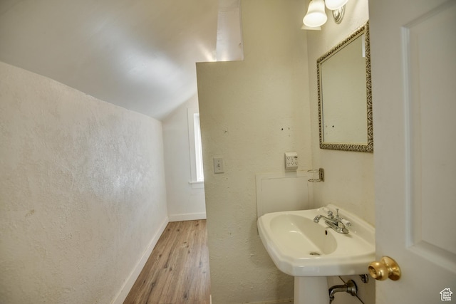 bathroom featuring baseboards, a sink, a textured wall, wood finished floors, and lofted ceiling