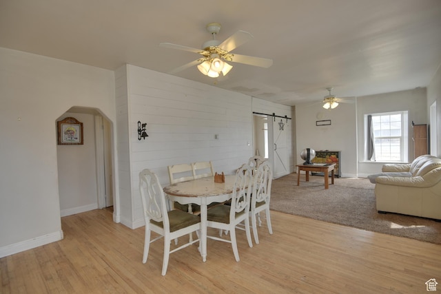 dining space featuring ceiling fan, light wood-style flooring, arched walkways, a barn door, and baseboards