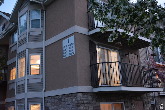 view of side of property featuring stone siding, a balcony, and stucco siding