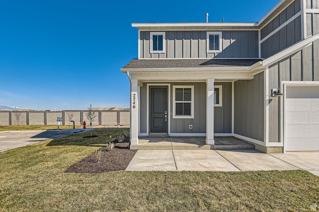 property entrance featuring board and batten siding, a garage, a yard, fence, and a shingled roof