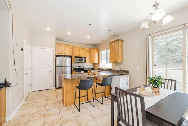 kitchen with dark stone counters, recessed lighting, a sink, stainless steel appliances, and light brown cabinets