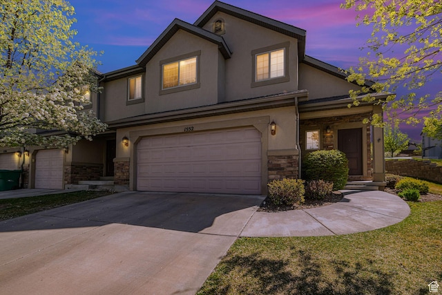 traditional home featuring an attached garage, stone siding, driveway, and stucco siding