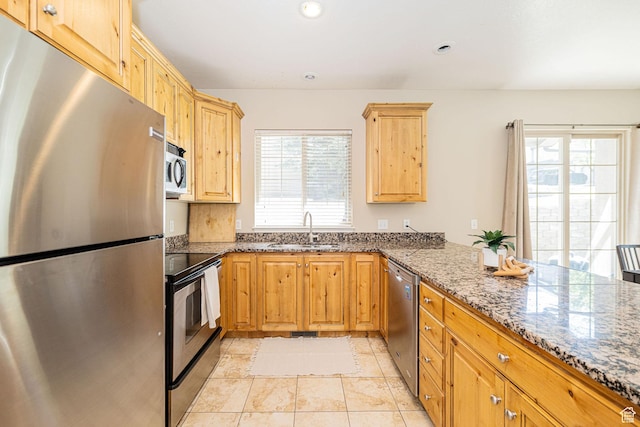 kitchen featuring stone counters, recessed lighting, a peninsula, appliances with stainless steel finishes, and a sink