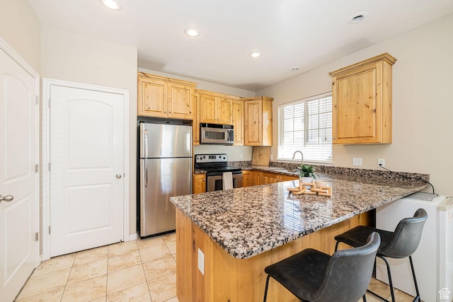 kitchen with a kitchen breakfast bar, a peninsula, dark stone countertops, a sink, and stainless steel appliances