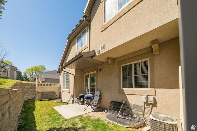 rear view of house with central AC unit, a patio area, a yard, fence, and stucco siding