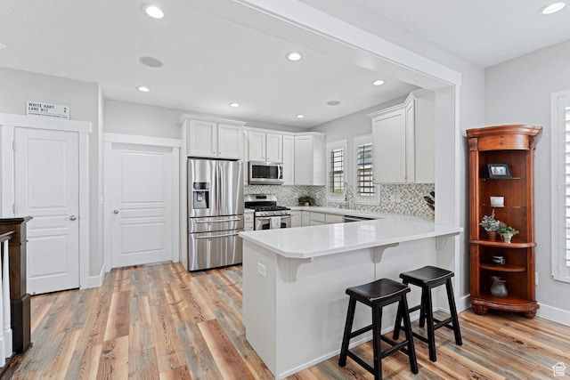 kitchen with stainless steel appliances, light wood-type flooring, a breakfast bar area, white cabinetry, and a peninsula