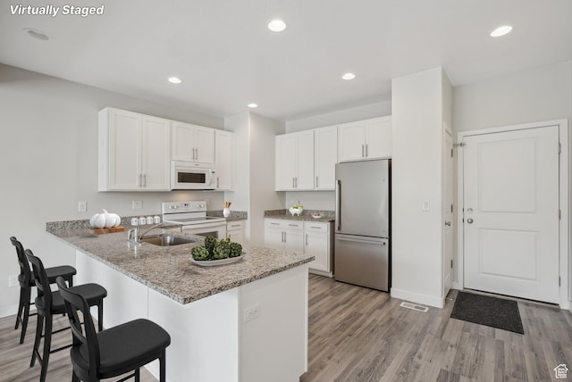 kitchen featuring white cabinets, a sink, white appliances, and light wood-style floors